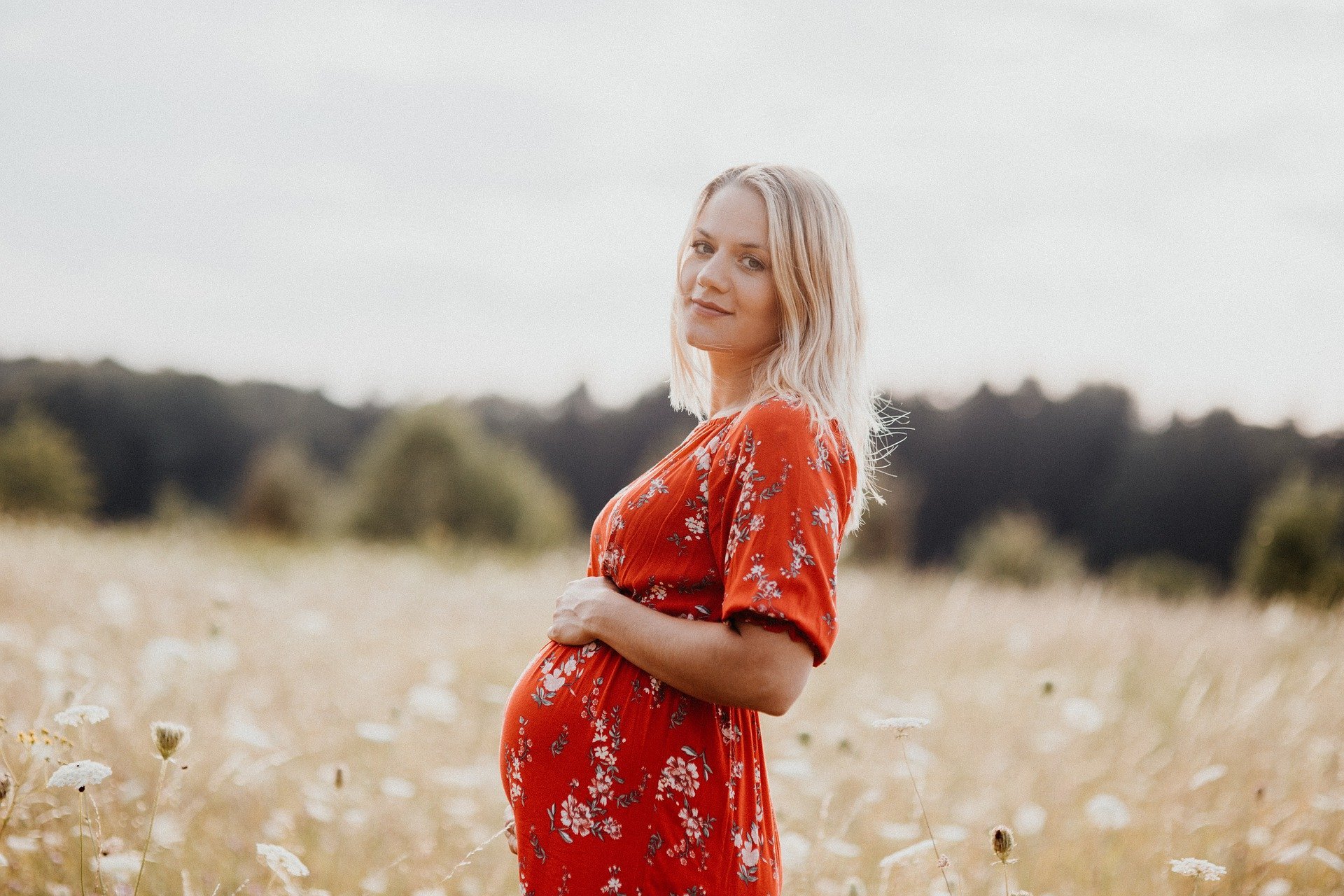 Pregnant woman with hands on belly in middle of green field.
