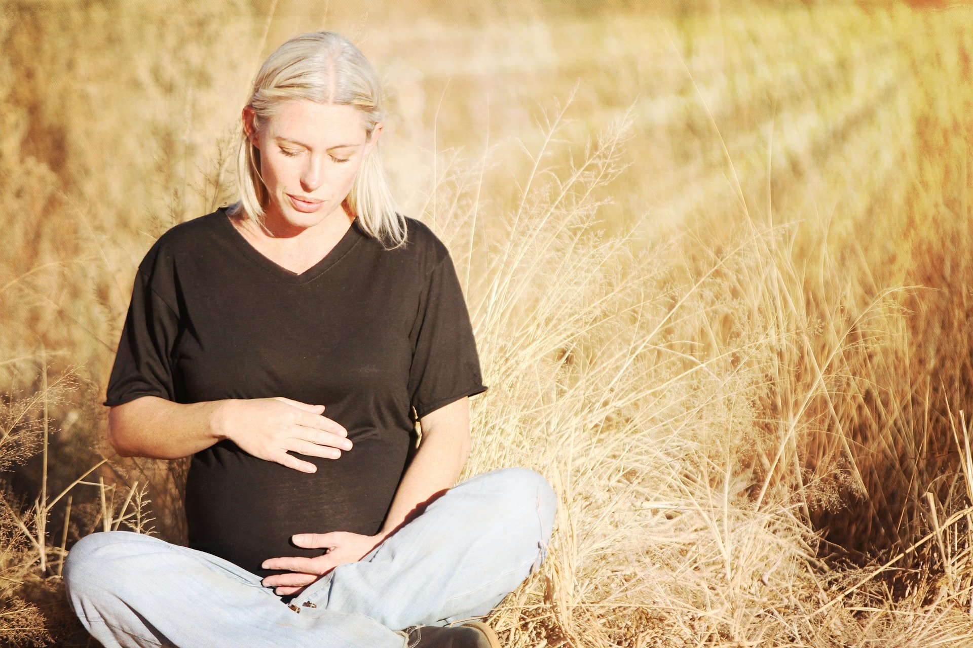 Pregnant woman with hands on her belly sitting in field.