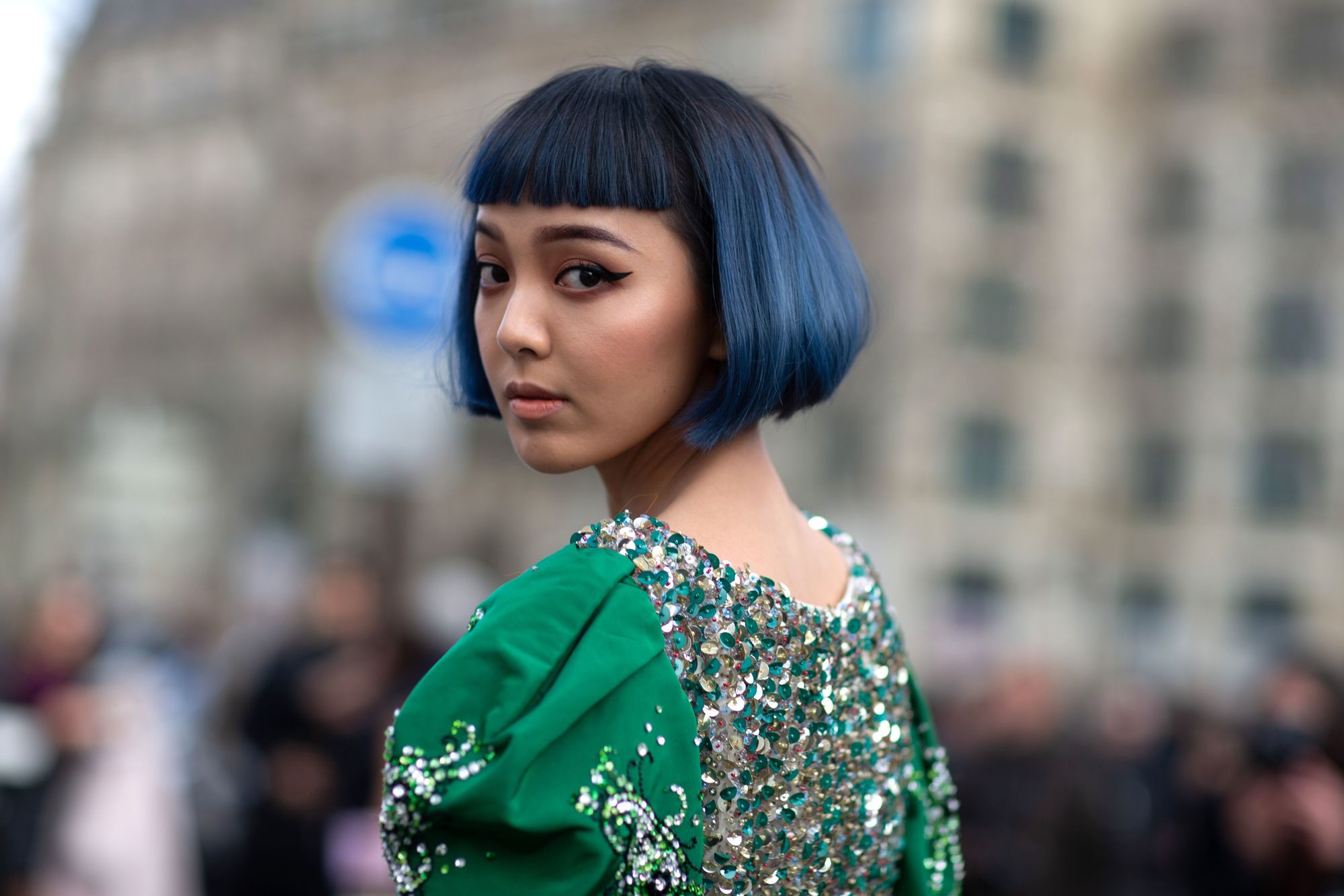 Woman with short hair, bangs and blue color oriental features looks back towards the camera.