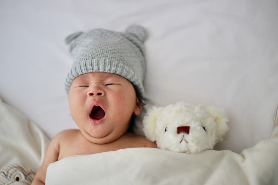 photo of yawning baby lying next to teddy bear