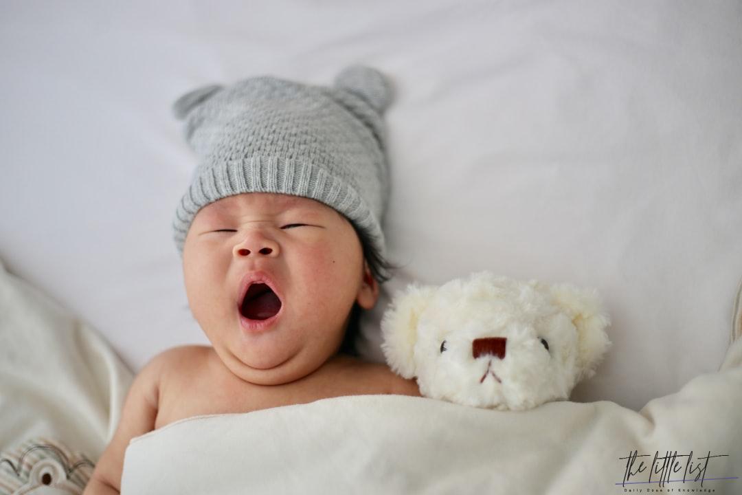 photo of yawning baby lying next to teddy bear