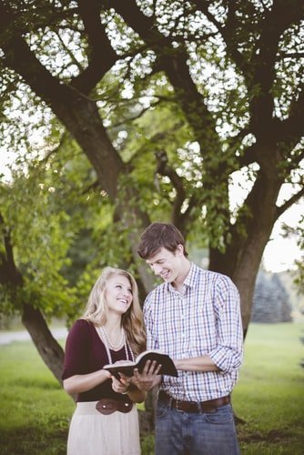 Couple reading the Bible and smiling under a tree.