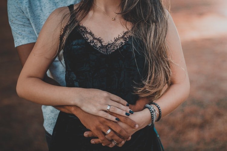 Man embracing woman and both hands clasped on her belly.