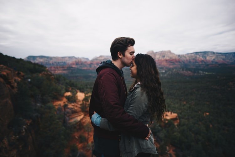 Man kissing woman's forehead and mountains in the background.