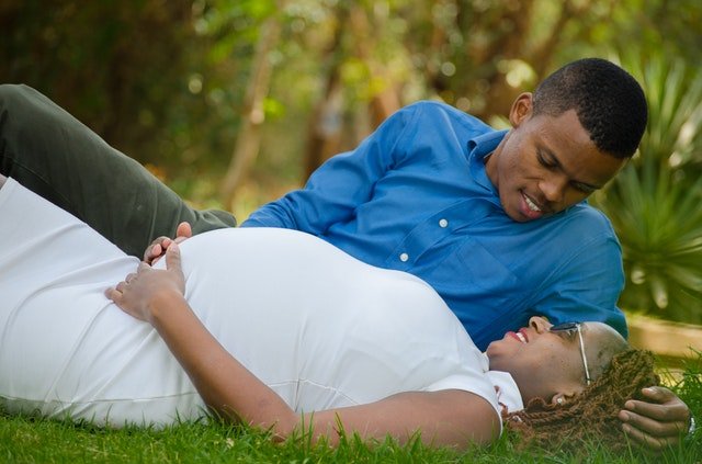 Black couple lying on the grass with their hands on the woman's belly.