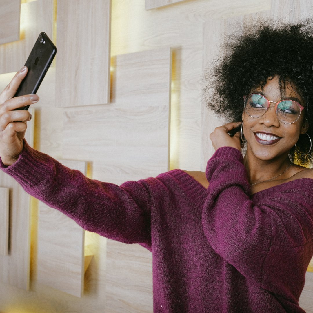 Woman with glasses smiling and taking a selfie.