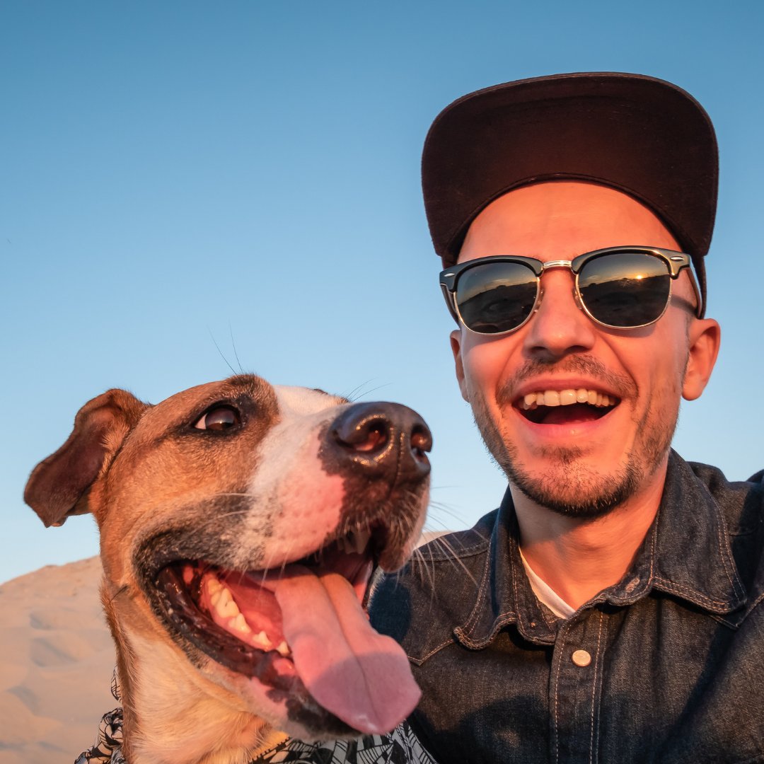 Man with sunglasses smiling and taking picture with a dog.