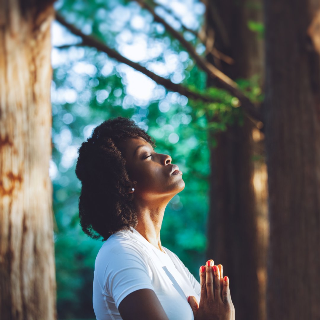 Woman with eyes closed and hands joined meditating in the forest.