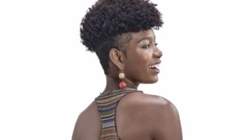 Model smiling in profile with short curly hair.
